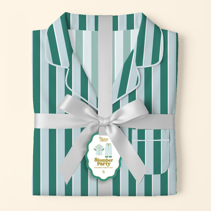 The Darling Effect’s Sicily Stripes Teal Slumber Party Pajama Pants Set, featuring teal and light blue stripes and crafted from ultra-soft fabric, is tied with a silver ribbon and a “Slumber Party Pajama Set” tag on a pale background.