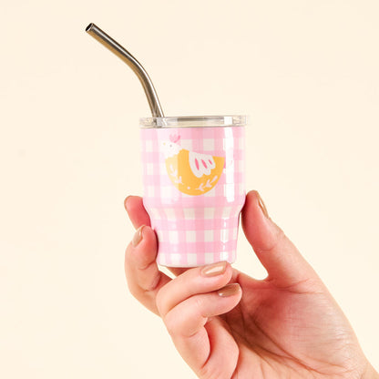 A hand holds the-darling-effect's Spring Chicken 2 oz Tiny Tumbler, a small pink and white gingham insulated shot glass with a metal straw and a cute chicken illustration with leaves, set against a plain light background.