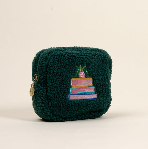 The Darling Effect Square Book Nook Teddy Pouch is a soft, dark green sherpa pouch with a zipper, gold charm, and embroidered stacked books topped by a pink potted plant—an adorable accessory for your collection.