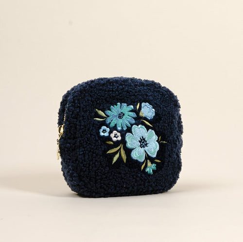 The Square Dainty Floral Navy Teddy Pouch by the-darling-effect is a navy blue sherpa cosmetic bag, adorned with embroidered blue and green flowers.