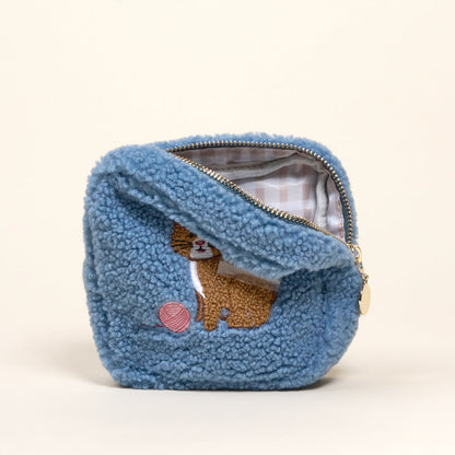The Darling Effect’s Square Kitty Corner Teddy Pouch is a small blue sherpa pouch with a zipper, featuring an embroidered cat with a pink yarn ball and a light plaid lining—ideal for any teddy pouches accessory set.