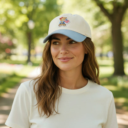 A woman with wavy brown hair, wearing a white t-shirt and The Darling Effect’s Star Spangled Bear Classic Canvas Hat, smiles softly while standing in a sunlit park.