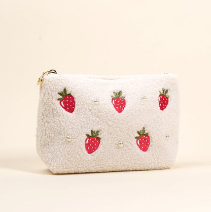 The Darling Effect Strawberries & Pearls Teddy Pouch features fluffy white sherpa, embroidered strawberries, and faux pearls—an adorable cosmetic bag to charm any accessory set.