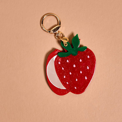The Darling Effect Strawberry Mini Mirror Bag Charm features a glittery red strawberry with green leaves and a silver acrylic mirror slice on a gold keyring—an eye-catching accessory for your bag.
