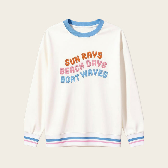 The Darling Effect’s Sun Rays, Beach Days, Boat Waves Oversized Crew features blue, pink, and orange text on beige with blue collar and cuffs detailed in pink and white stripes—a cozy wardrobe staple.