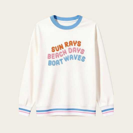 The Darling Effect’s Sun Rays, Beach Days, Boat Waves Oversized Crew features blue, pink, and orange text on beige with blue collar and cuffs detailed in pink and white stripes—a cozy wardrobe staple.