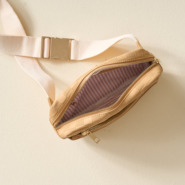 The Darling Effect’s Tan Urban Check Belt Bag, featuring beige checkered vegan leather, a cream strap, and gold buckle, sits unzipped on a light surface to reveal its pink and white striped fabric lining.