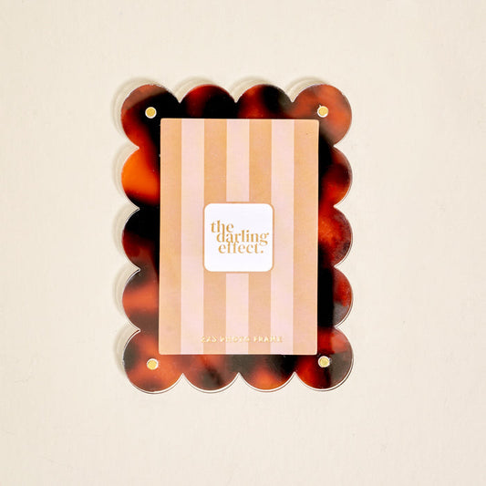 The Darling Effect's Tortoise Mini Acrylic Picture Frame Magnet features a scalloped tortoiseshell design and rounded edges, perfect for displaying photos on your fridge against a plain light background.