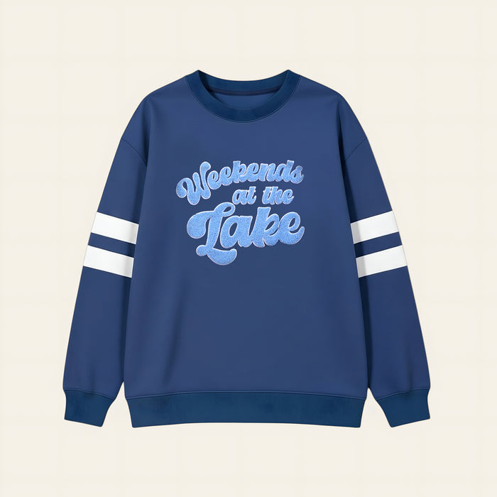 The Darling Effect's Weekends at the Lake Oversized Crew is a cozy blue sweatshirt with white sleeve stripes and "Weekends at the Lake" in large light blue script—ideal for relaxing by the water.