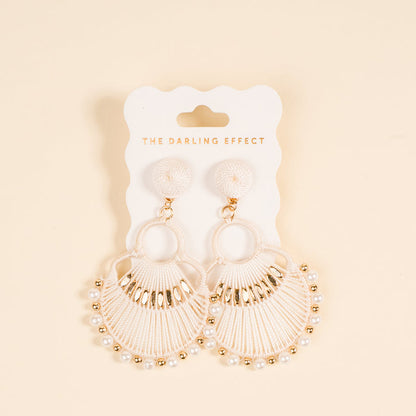 The Darling Effect White Paloma Drop Earrings showcase a fan-shaped woven design with pearl-like beads and gold accents, displayed on a branded card—stylish, lightweight statement earrings against a light beige background.