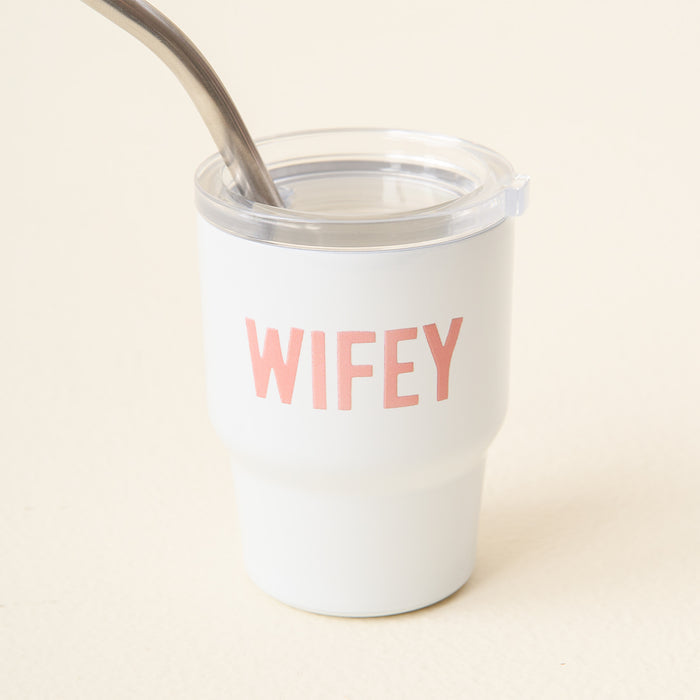 The-darling-effect’s Wifey 2 oz Tiny Tumbler features “WIFEY” in pink on a white insulated cup, with a clear lid and metal straw, shown against a plain light background.