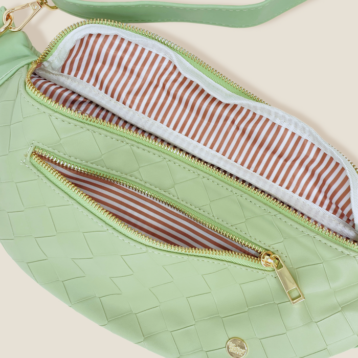The Darling Effect’s Woven Sage Trendy Luxe Belt Bag features vegan leather in light green with gold zippers, a matching strap for hands-free style, an exterior zip pocket, and is lined with brown and white striped fabric.