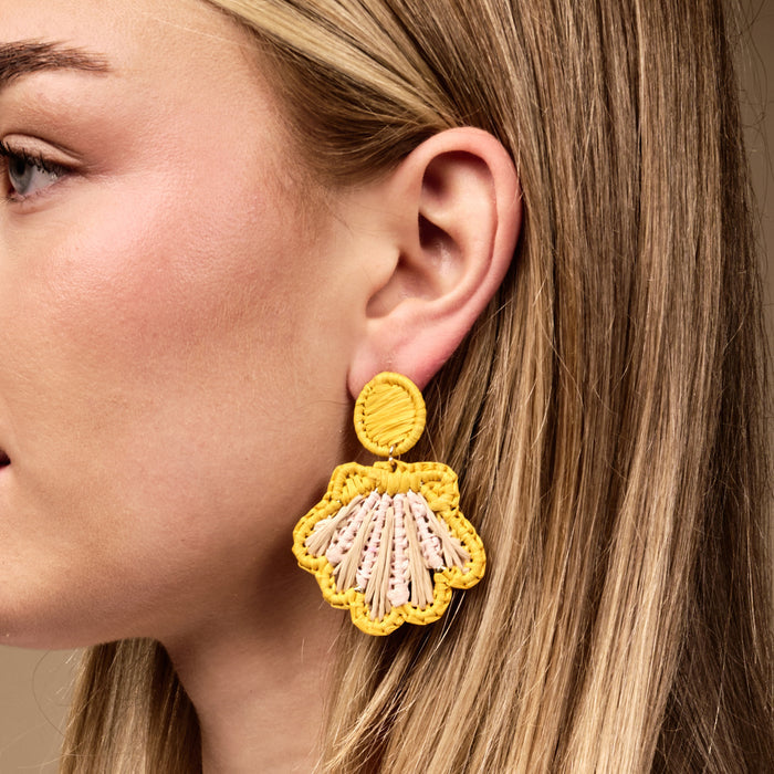 Close up of a woman's ear wearing The Darling Effect's Yellow Cabana Breeze Earrings—yellow shell-shaped boho pieces with pink and tan accents that are lightweight and perfect for everyday wear.