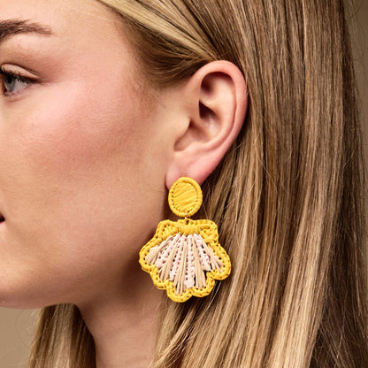 Close up of a woman's ear wearing The Darling Effect's Yellow Cabana Breeze Earrings—yellow shell-shaped boho pieces with pink and tan accents that are lightweight and perfect for everyday wear.