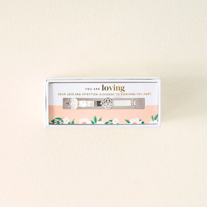 The Darling Effect’s You Are Loving Skinny Stacker Bracelet, a silver adjustable cuff with floral designs, arrives in a gift-ready box that reads “You are loving,” with flowers decorating the inside.