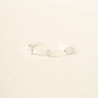 The Darling Effect's You Are Loving Skinny Stacker Bracelet—a minimalist silver adjustable cuff with three circular floral designs—is an elegant, gift-ready accessory styled on a light cream textured surface.