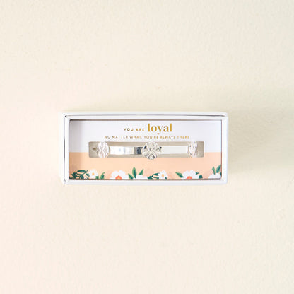 Gift-ready in a white box, The Darling Effect's "You Are Loyal" Skinny Stacker Trait Bracelet is a silver adjustable cuff with floral engravings. The lid reads, "YOU ARE loyal" and has a floral design at the bottom.