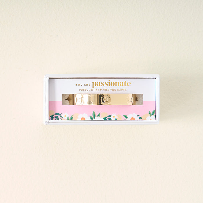 The Darling Effect’s You Are Passionate Cuff Bracelet features gold charms and comes boxed with floral-bordered packaging that reads, “You are passionate. Pursue what makes you happy,” set against a light background.