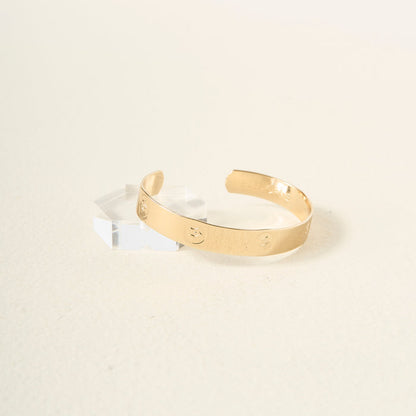 The Darling Effect’s You Are Passionate Cuff Bracelet, featuring engraved circular motifs, sits on a light surface next to a clear acrylic block, highlighting the timeless style of this adjustable accessory.