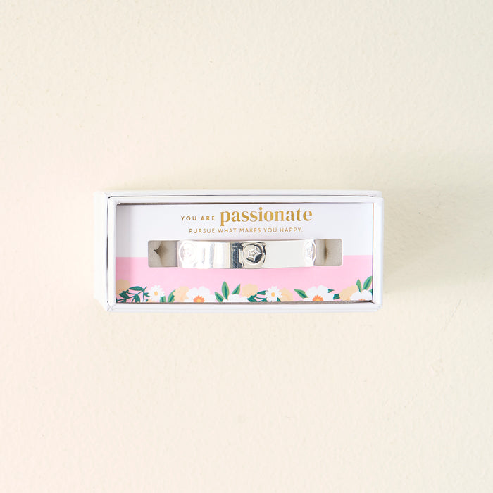 The Darling Effect's "You Are Passionate" Cuff Bracelet is a sterling silver adjustable piece, boxed with a floral design and the message “You are passionate. Pursue what makes you happy.” printed on a pink background inside.
