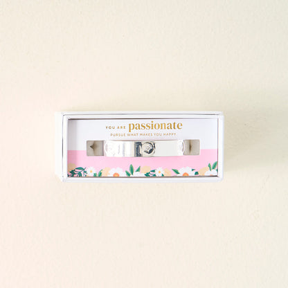 The Darling Effect's "You Are Passionate" Cuff Bracelet is a sterling silver adjustable piece, boxed with a floral design and the message “You are passionate. Pursue what makes you happy.” printed on a pink background inside.