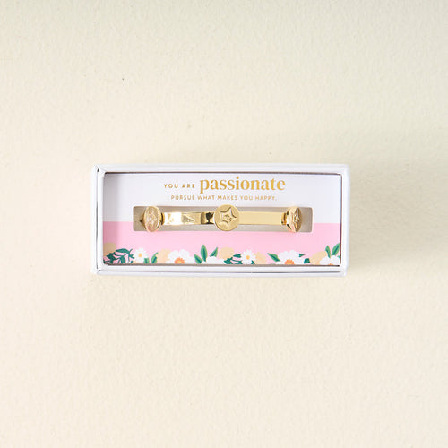 The Darling Effect’s You Are Passionate Skinny Stacker Bracelet features a 14k gold plated adjustable cuff with star and heart charms, presented in a floral-accented gift box. The lid reads: You are passionate. Pursue what makes you happy.