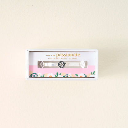 The Darling Effect’s You Are Passionate Skinny Stacker Bracelet is a silver adjustable cuff with star and heart designs, gift-boxed on a floral card reading “You are passionate. Pursue what makes you happy”—perfect for gifting.